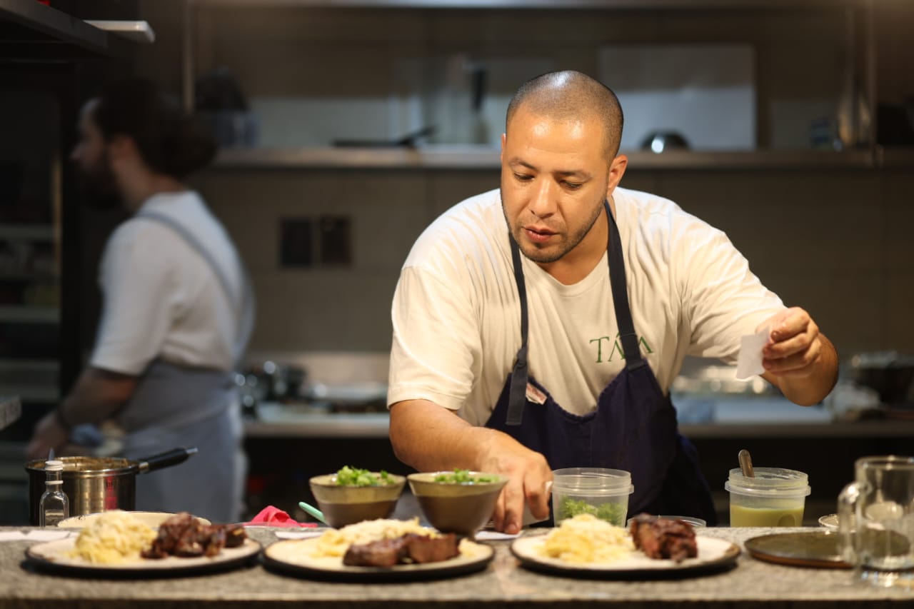 A chef meticulously plating a colorful, modern Paraguayan dish with tweezers in a bright, professional kitchen. minimalist style